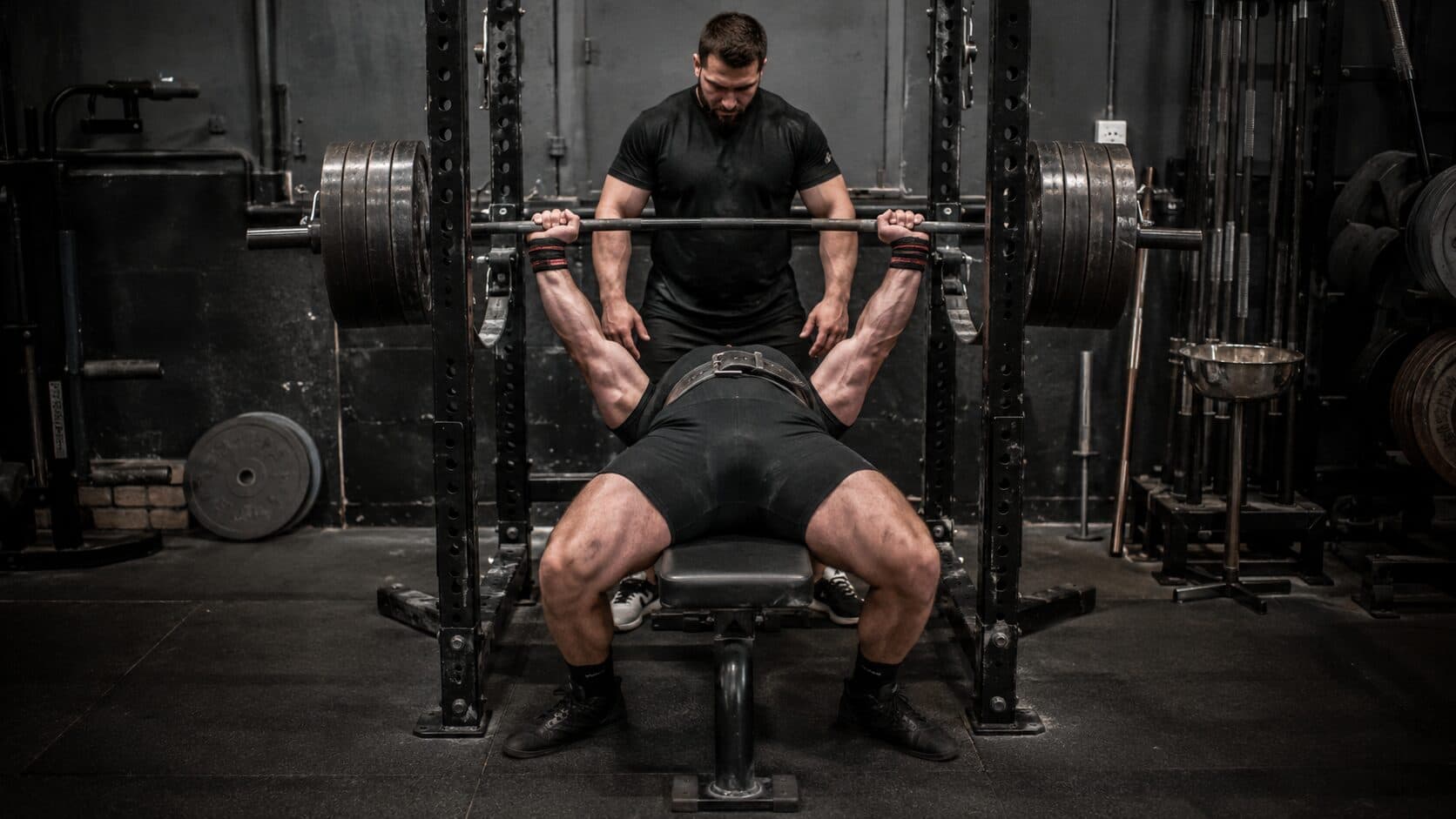 A lifter setting a personal record on the bench press with a spotter in a weight room